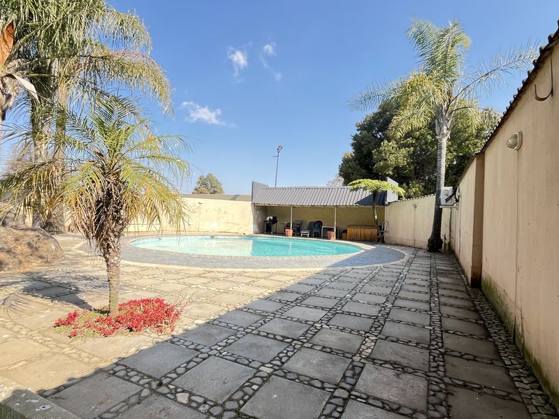 Outdoor pool area featuring a circular swimming pool, paved surround, and a covered entertainment structure enclosed by a perimeter wall.