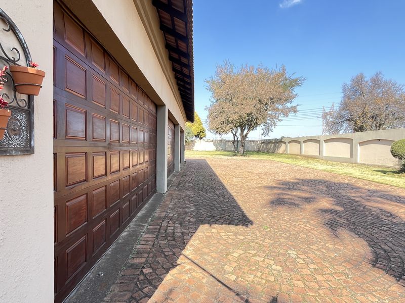 Front exterior view of the property featuring a double garage with wooden doors, a paved driveway, and a secure perimeter wall.