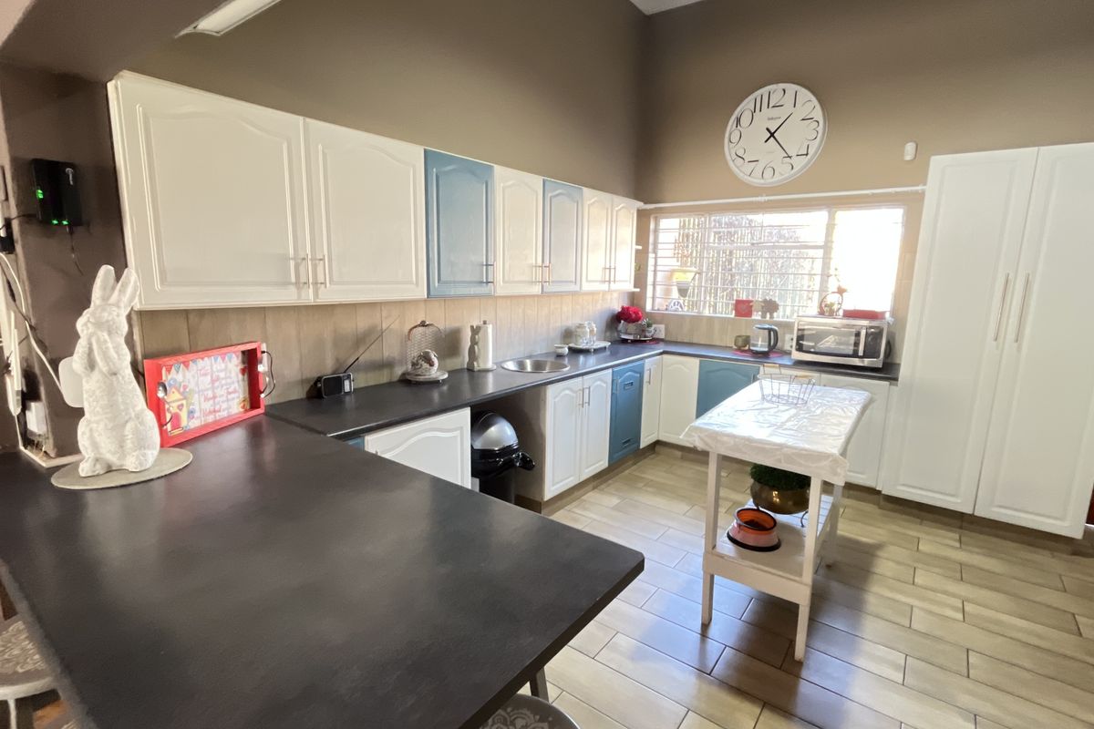 A functional kitchen featuring white and blue cabinetry, dark laminate countertops, tiled flooring, and a window with security bars.