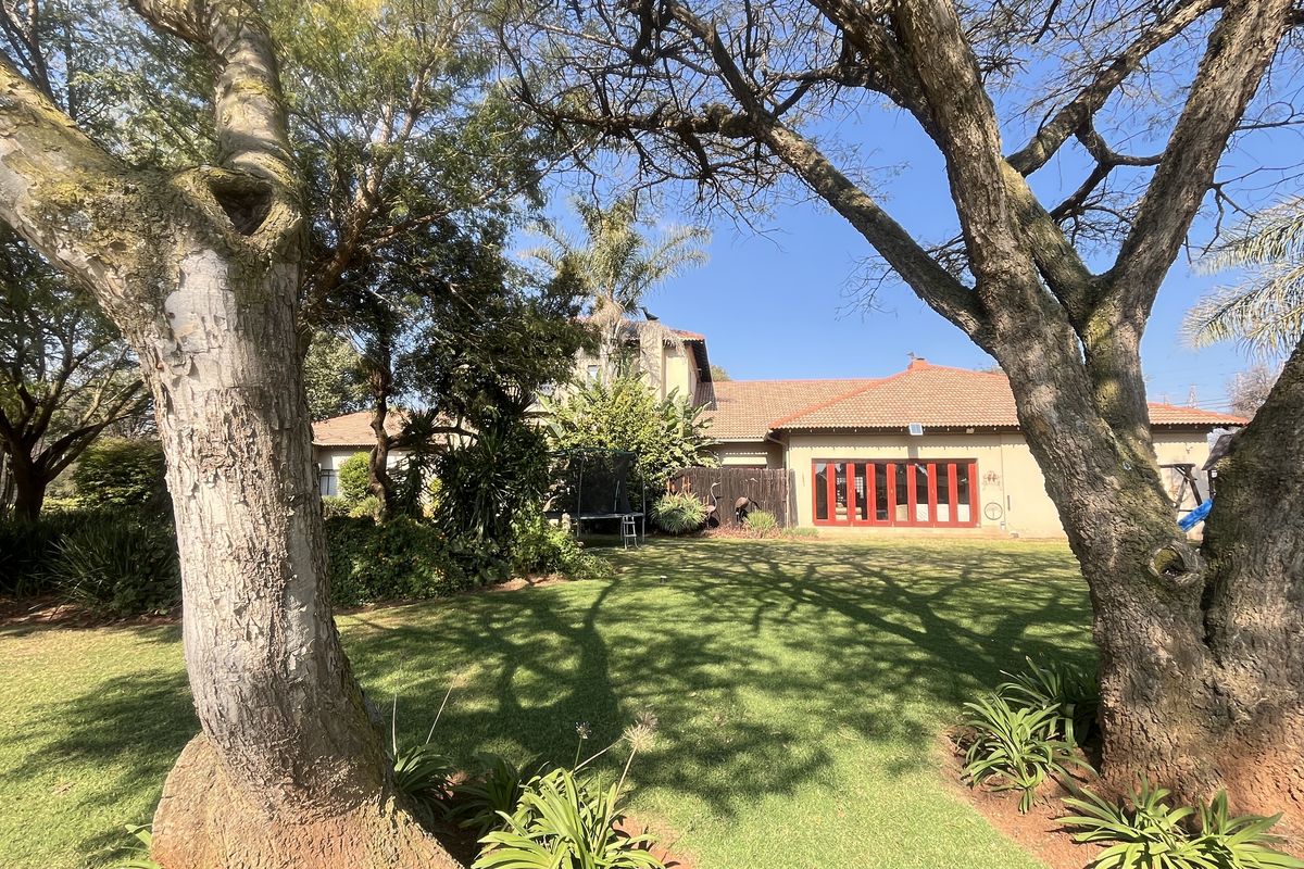 Rear view of the property featuring a well-maintained garden, mature trees, and red-framed folding doors leading into the home.