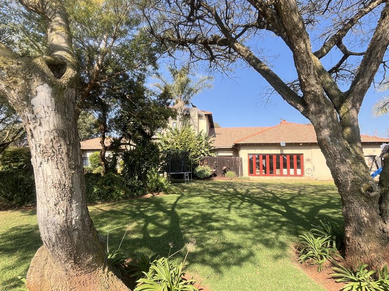 Rear view of the property featuring a well-maintained garden, mature trees, and red-framed folding doors leading into the home.
