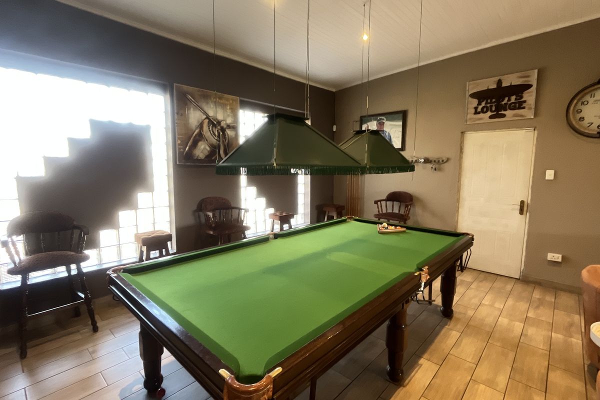 A spacious entertainment room featuring tiled flooring, glass block windows, and dedicated billiard lighting, currently set up as a recreational lounge area.