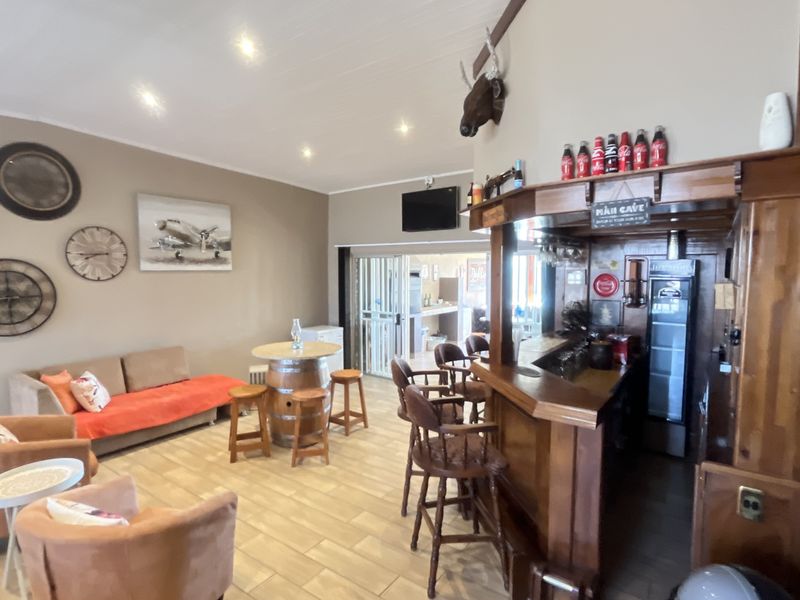 A rustic-style bar area featuring a built-in wooden counter, tiled flooring, recessed lighting, and an exposed brick feature wall.