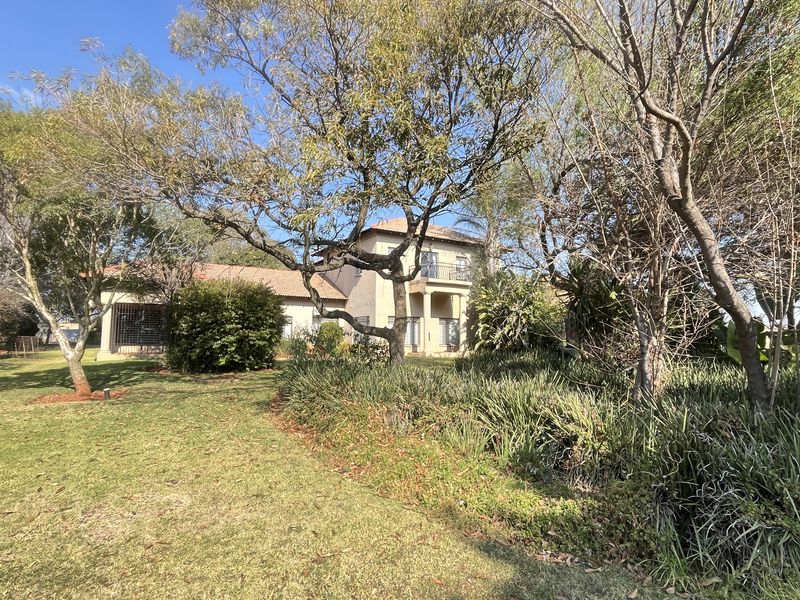 A view of the rear elevation of the property featuring a multi-story structure with a balcony, set within a spacious, mature garden.