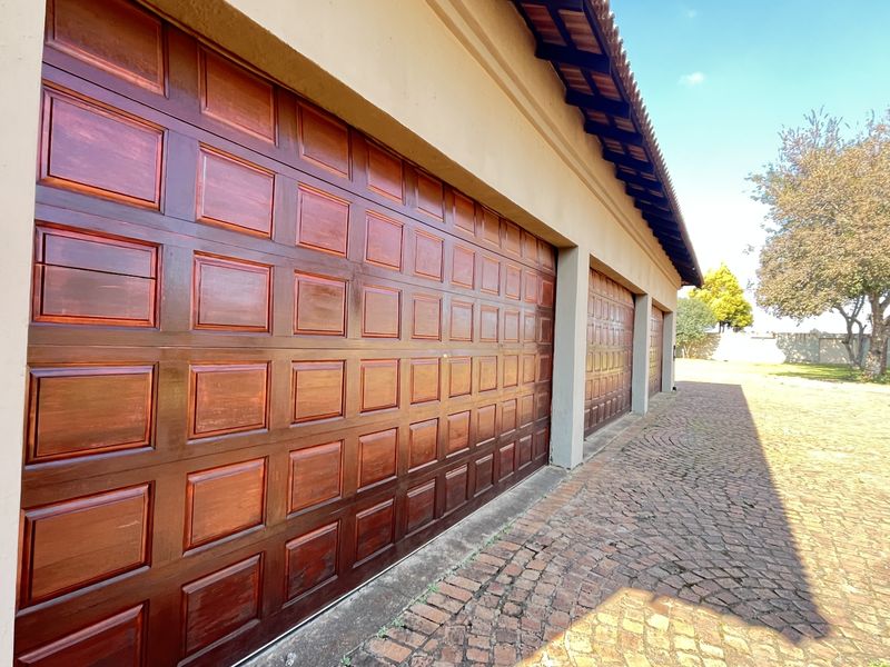 Exterior view of a triple garage with wooden panel doors and a paved driveway on a small holding property.