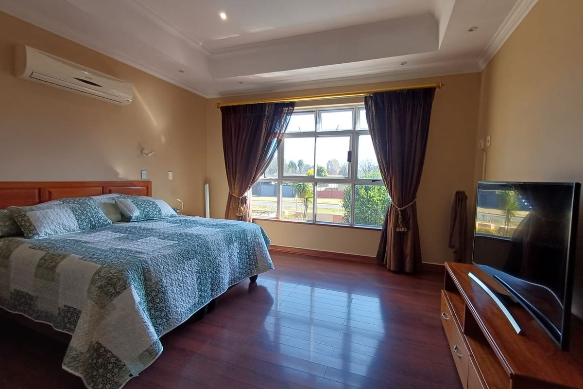Spacious bedroom featuring laminate flooring, recessed ceiling with downlights, and a wall-mounted split-system air conditioner.
