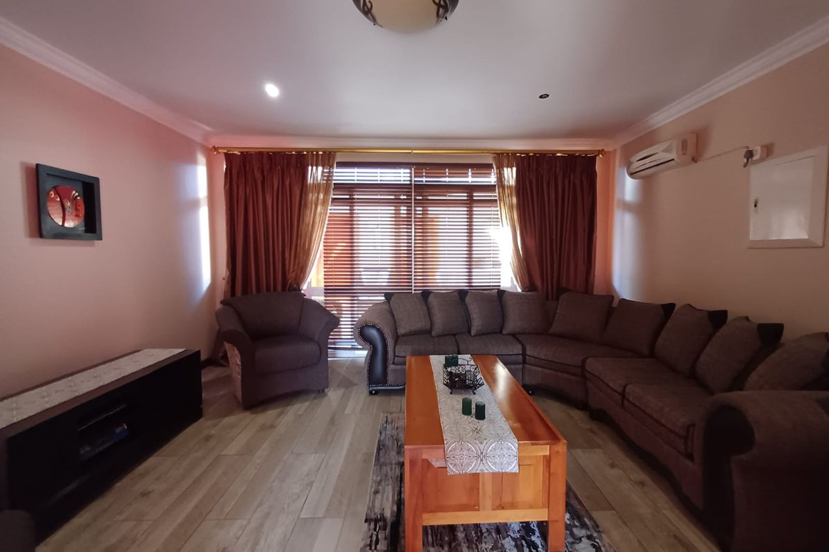 A comfortable living room featuring wood-look tile flooring, a split-system air conditioner, and large windows with venetian blinds.