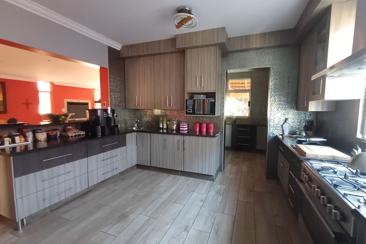 Modern kitchen featuring wood-grain cabinetry, granite countertops, a gas hob with extractor, and durable tiled flooring, offering a functional and contemporary cooking space.