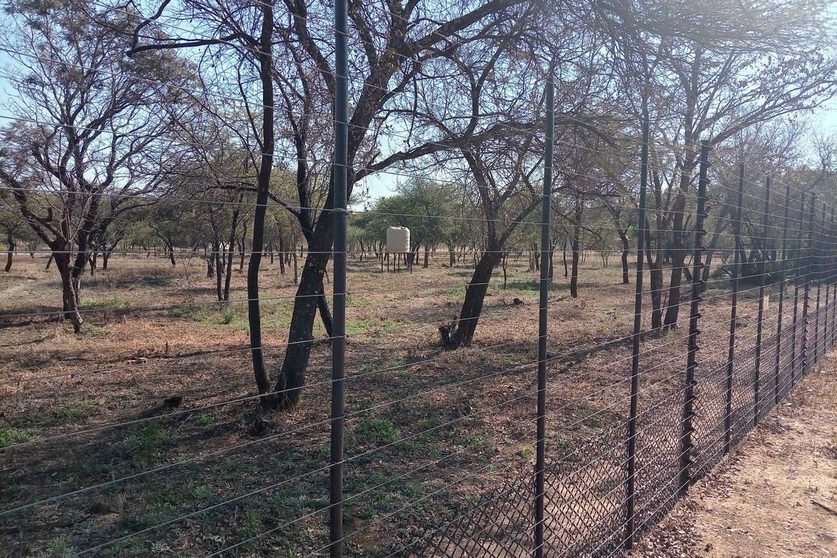 A view of the farm grounds featuring a secure perimeter electric fence and a raised water storage tank set among mature trees.