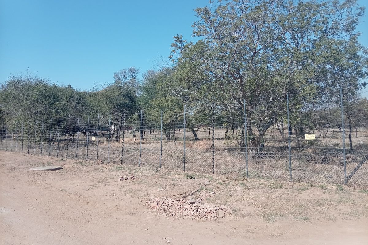 A view of the farm property boundary featuring secure wire mesh and electric fencing surrounding a natural landscape with mature trees.
