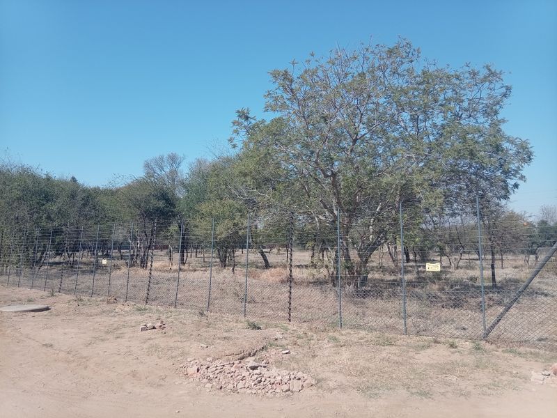 A view of the farm property perimeter featuring wire mesh fencing with integrated electric security wires and mature trees.