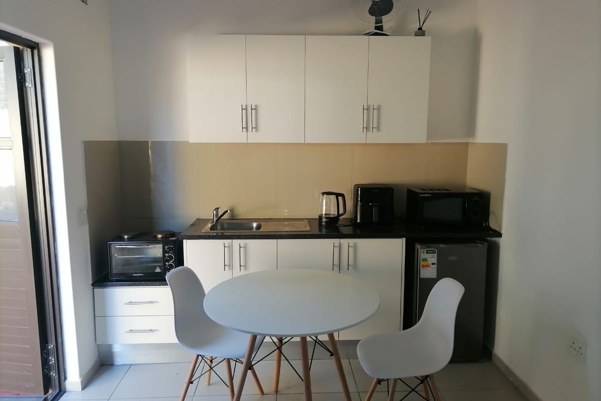 Compact kitchen area featuring white built-in cabinetry, a dark laminate countertop, stainless steel sink, and tiled backsplash, suitable for efficient apartment living.