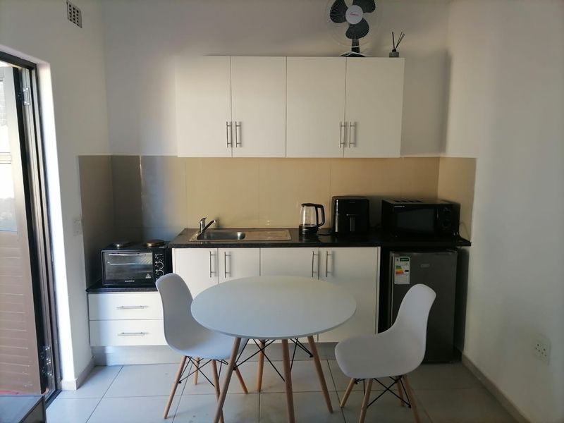 Compact kitchen area featuring white built-in cabinetry, a dark laminate countertop, stainless steel sink, and tiled backsplash, suitable for efficient apartment living.