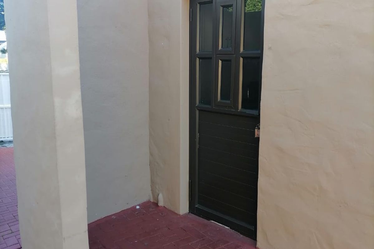A rear exterior view showing a paved patio area leading to a dark timber door with glass panels.