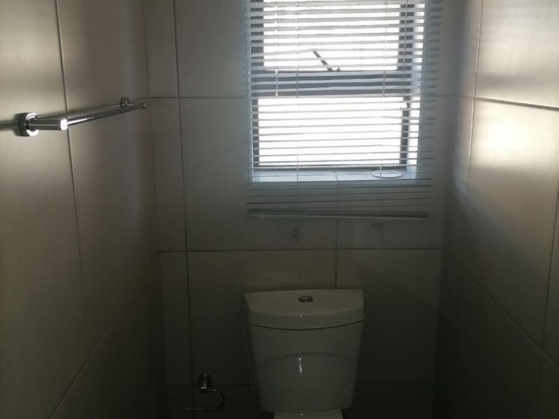 A compact bathroom featuring tiled walls, a standard toilet, and a window with fitted blinds.