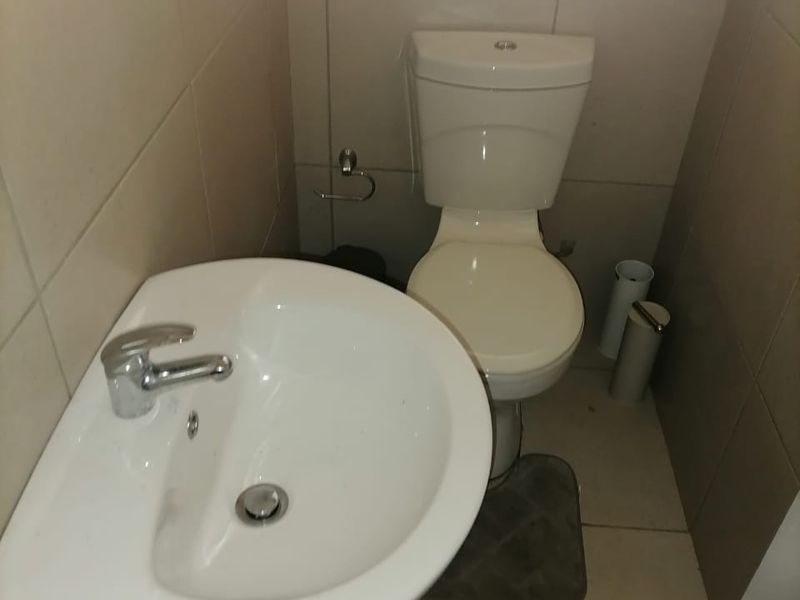 A compact bathroom featuring a white pedestal basin, a standard toilet, and neutral wall and floor tiling.