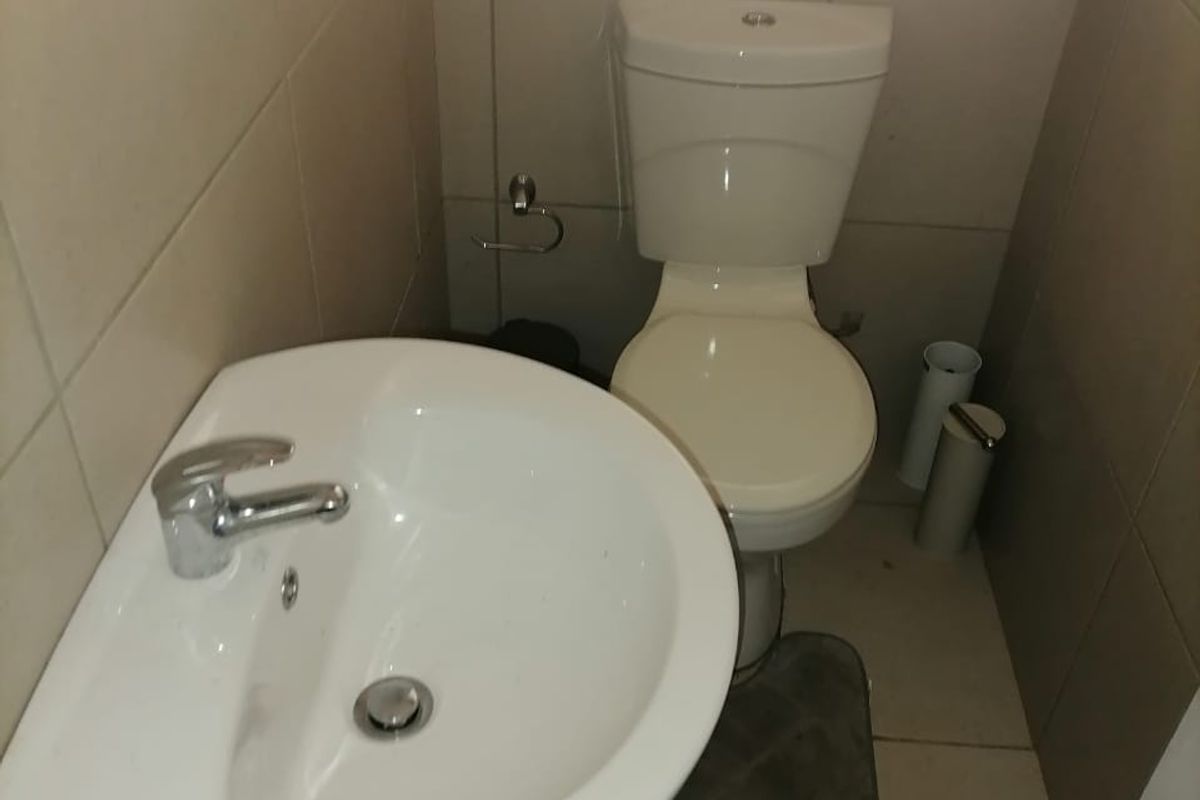 A compact bathroom featuring a white pedestal basin, a standard toilet, and neutral wall and floor tiling.