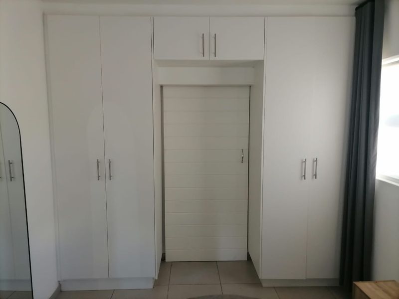 A bedroom featuring clean white built-in cupboards with overhead storage and a modern sliding door, set against neutral tiled flooring.