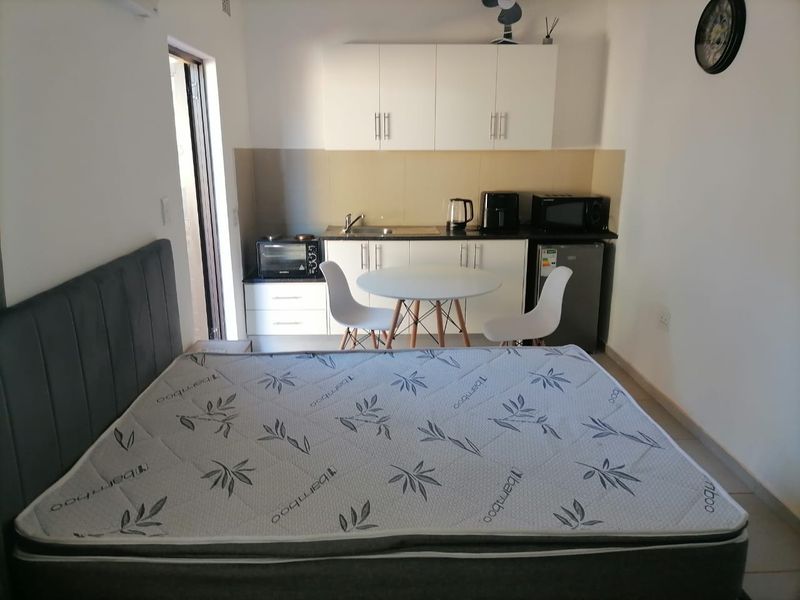 An open-plan studio apartment featuring a compact kitchenette with built-in cabinetry, sink, and tiled splashback, integrated into the main living and sleeping area.