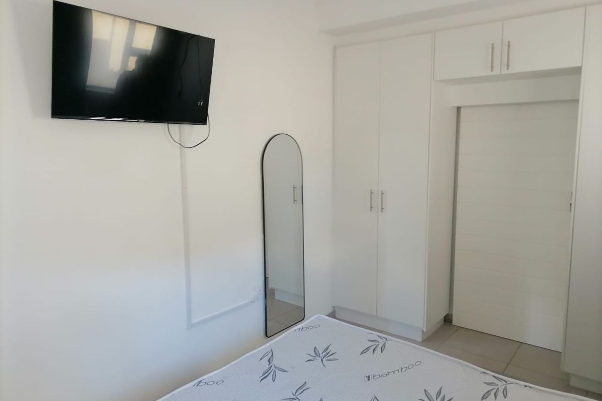A clean bedroom featuring white built-in wardrobes with overhead storage and tiled flooring.