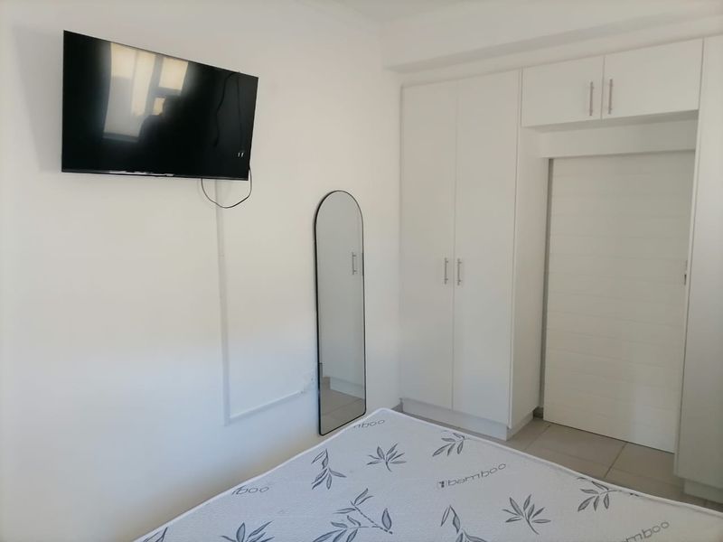 A clean bedroom featuring white built-in wardrobes with overhead storage and tiled flooring.