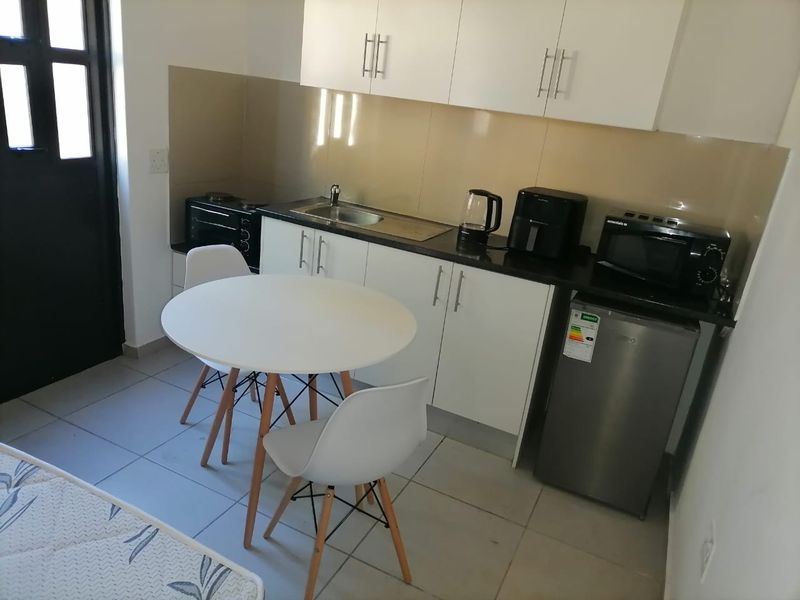 Compact kitchen area featuring white cabinetry, dark countertops, stainless steel sink, and tiled flooring, suitable for efficient apartment living.