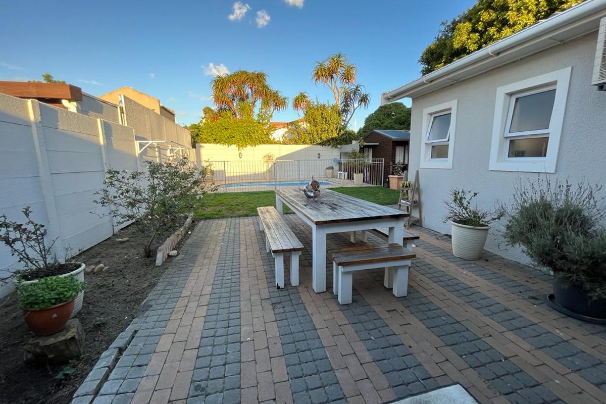 Rear garden area featuring a paved patio, swimming pool, and secure boundary walls, providing a functional outdoor space for relaxation and entertainment.