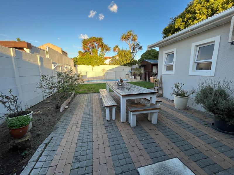 Rear garden area featuring a paved patio, swimming pool, and secure boundary walls, providing a functional outdoor space for relaxation and entertainment.