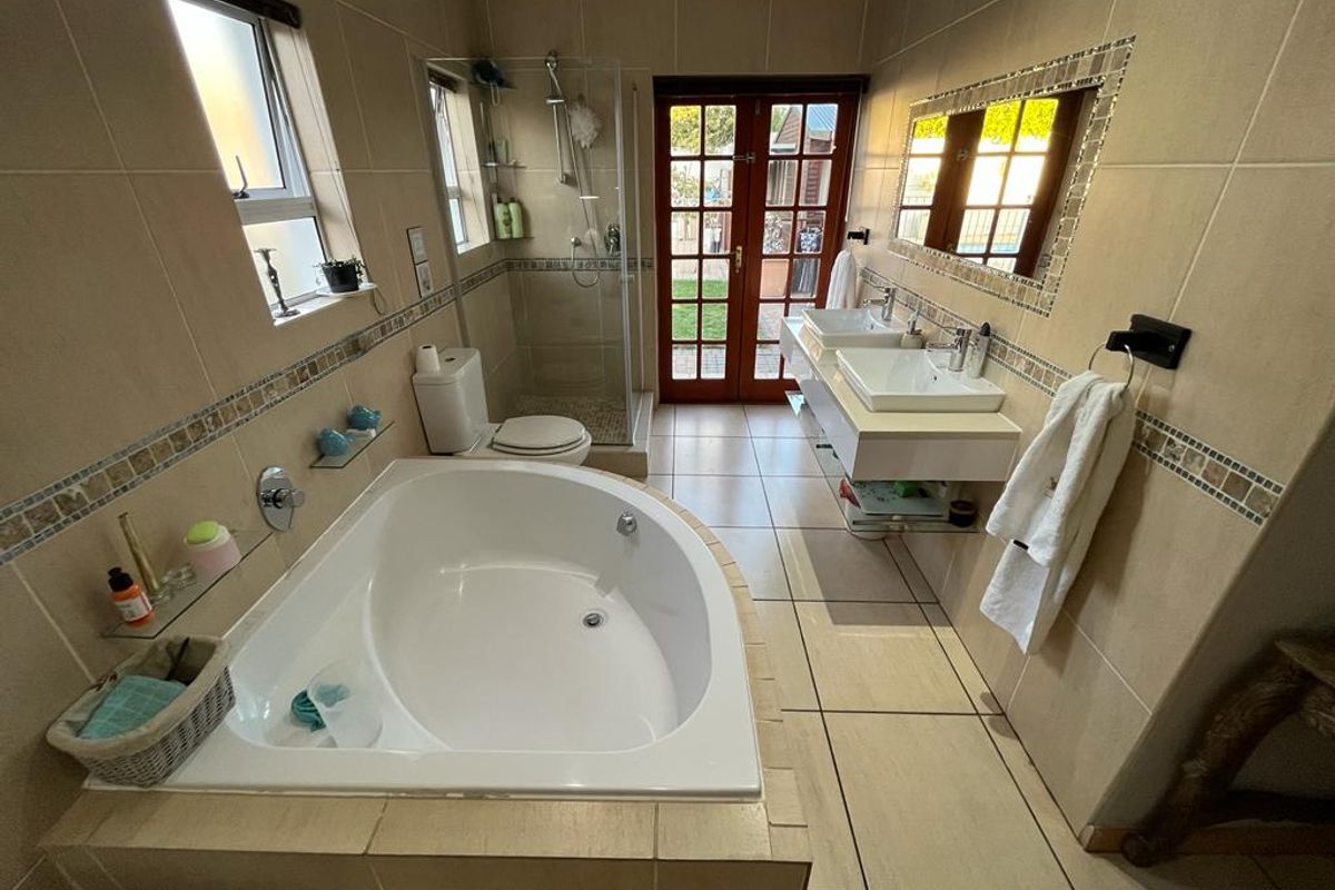 Spacious bathroom featuring a corner bathtub, glass shower enclosure, dual vanity sinks, and direct access to the outdoors through French doors.