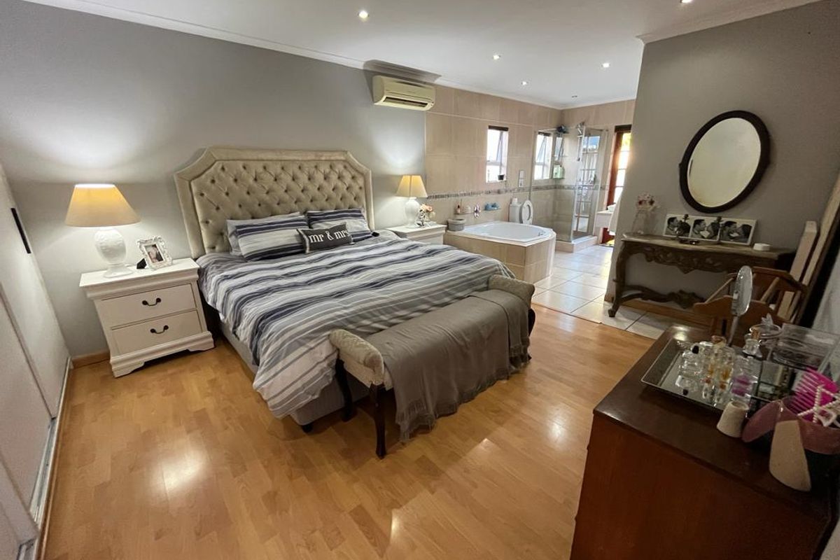 Spacious master bedroom featuring laminate flooring, recessed lighting, air conditioning, and an open-plan en-suite bathroom with a built-in bathtub and glass shower.