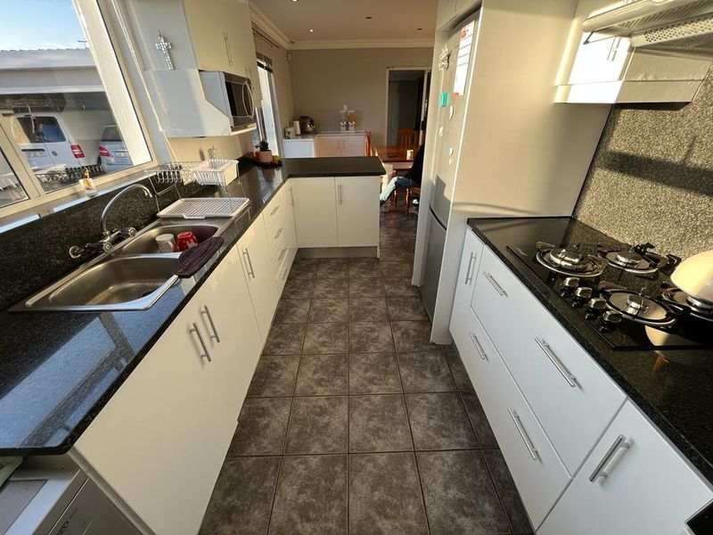 A functional kitchen featuring granite countertops, a double basin sink, built-in gas hob with extractor fan, and ample white cabinetry.