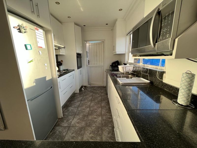 Functional galley-style kitchen featuring white cabinetry, dark granite countertops, built-in appliances, and tiled flooring with direct access to the exterior.