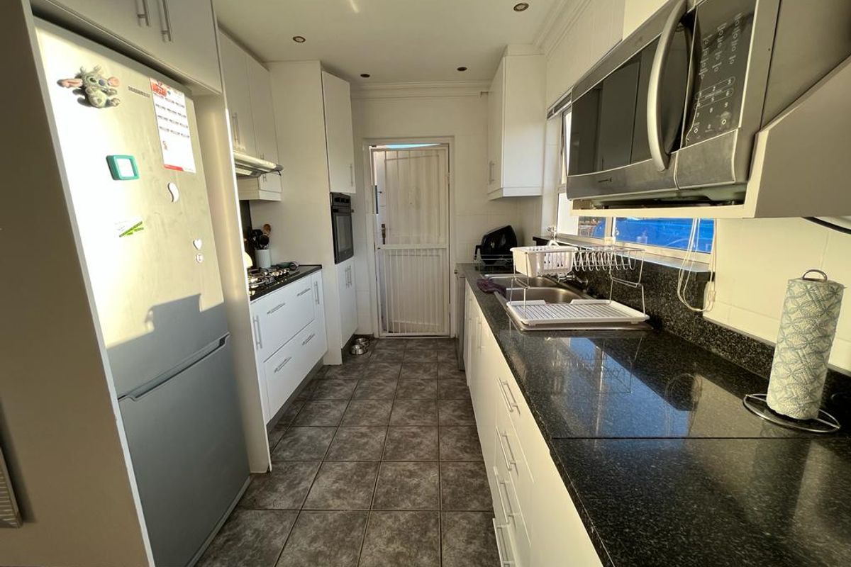 Functional galley-style kitchen featuring white cabinetry, dark granite countertops, built-in appliances, and tiled flooring with direct access to the exterior.