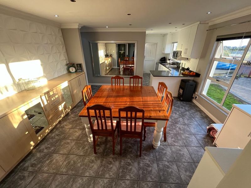 Spacious open-plan dining and kitchen area featuring tiled floors, modern built-in cabinetry, a textured feature wall, and ample natural light.