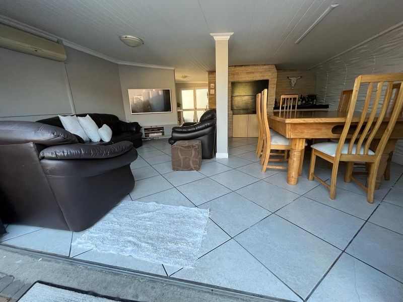 Open-plan living and dining area featuring tiled floors, a built-in braai, and an air conditioning unit, providing a versatile space for indoor entertainment.