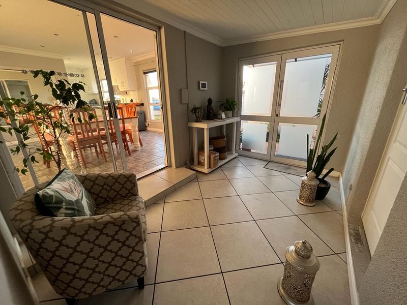 A bright, enclosed patio area featuring tiled flooring, recessed ceiling lights, and large glass doors providing seamless access to the interior living space.