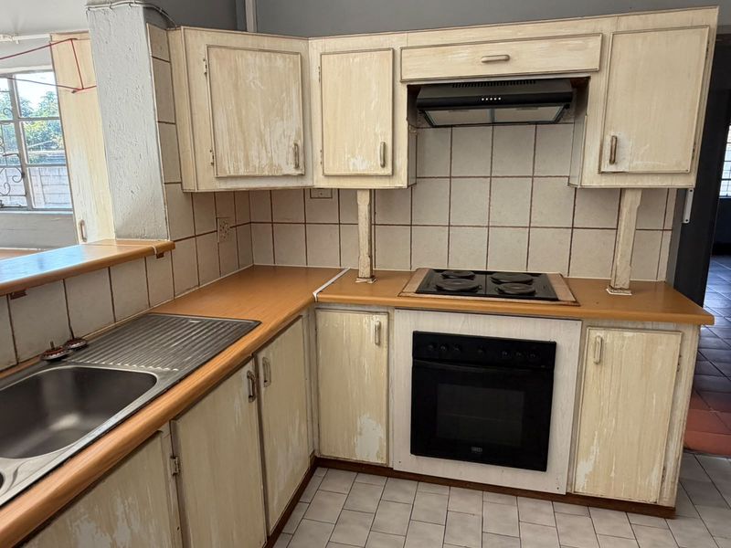 A functional kitchen featuring built-in cabinetry, laminate countertops, an electric hob, and an integrated oven, requiring cosmetic updates to modernize the space.
