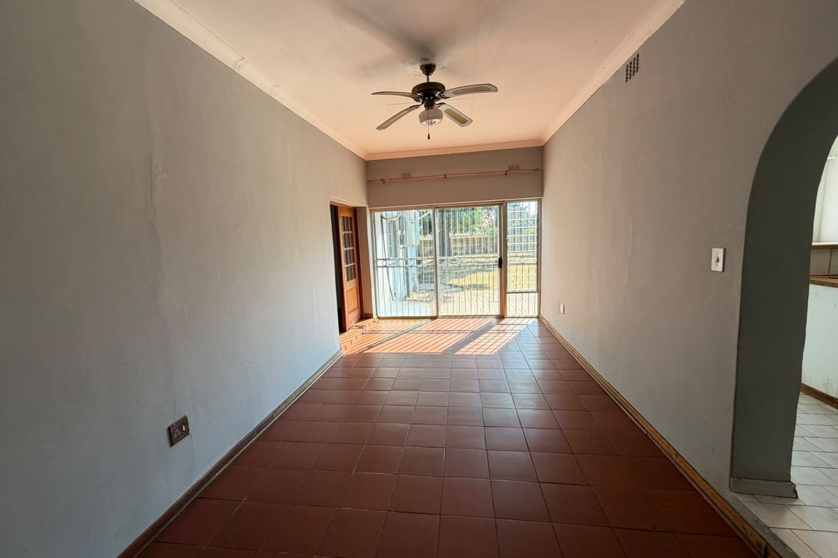 An empty living room featuring tiled flooring, a ceiling fan, and a sliding glass door providing access to the rear exterior.