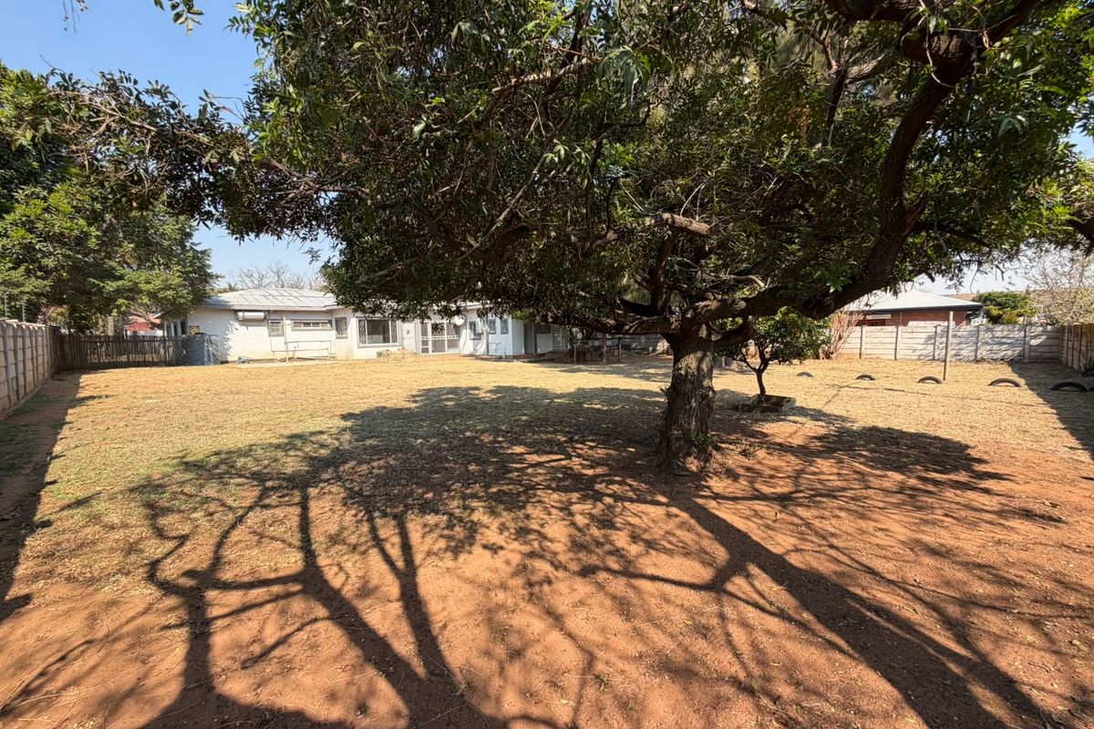 A spacious rear garden featuring a large mature tree, expansive lawn area, and perimeter precast concrete walling.