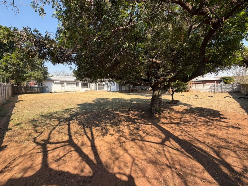 A spacious rear garden featuring a large mature tree, expansive lawn area, and perimeter precast concrete walling.