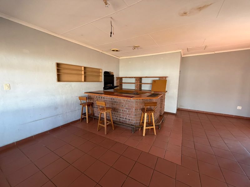 A dedicated bar area featuring a built-in brick counter, tiled flooring, and wall-mounted shelving, offering potential for renovation and modernization.