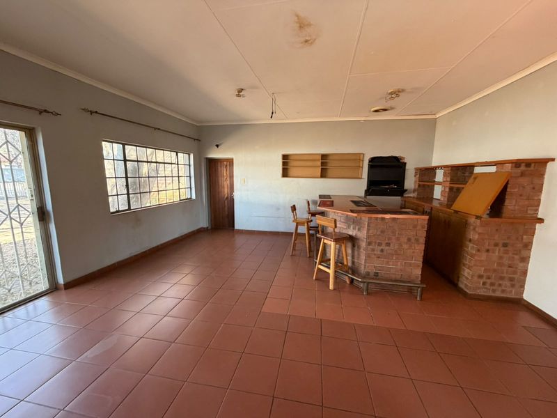 A spacious bar area featuring a built-in brick counter, tiled flooring, and steel-framed windows, requiring some ceiling and wall maintenance.