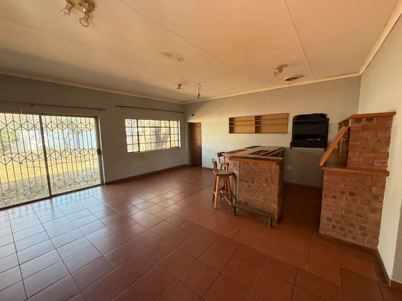 Spacious entertainment area featuring a built-in brick bar and fireplace, tiled flooring, and direct access to the garden through a sliding security door.