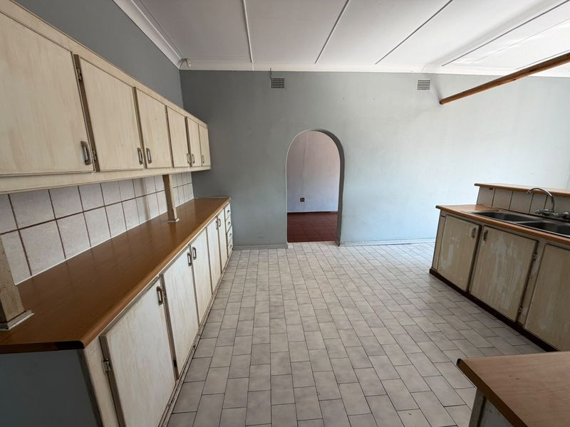 An empty, dated kitchen featuring extensive built-in cabinetry, laminate countertops, a double bowl sink, and tiled flooring, ready for a modern renovation.
