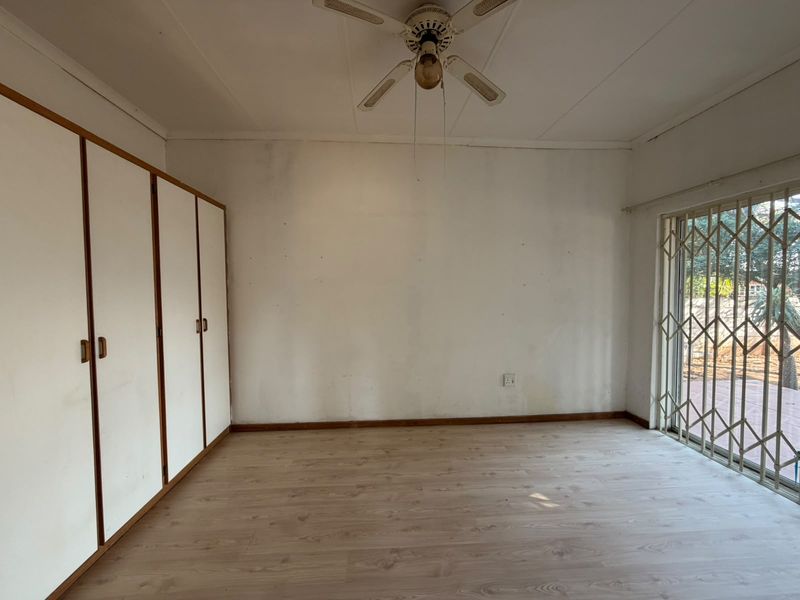 An empty bedroom featuring laminate flooring, built-in cupboards, a ceiling fan, and a security gate leading to the exterior.