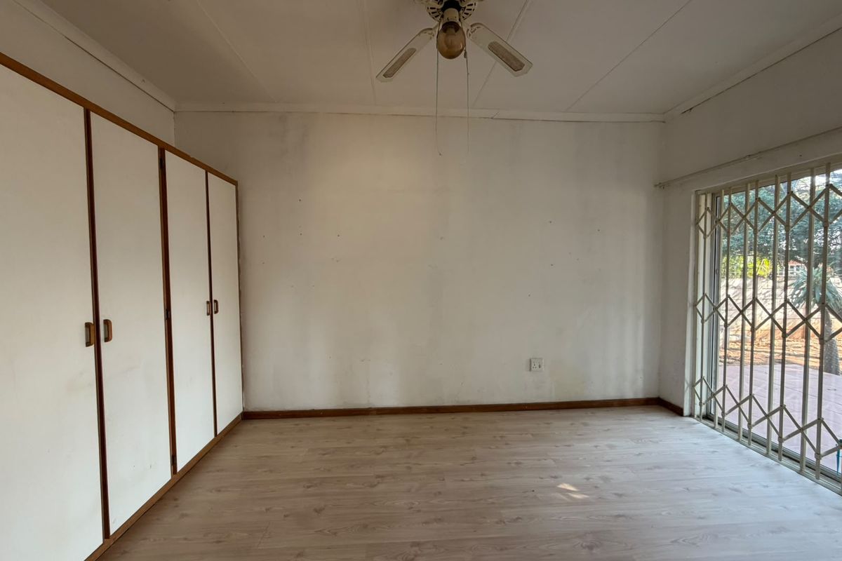 An empty bedroom featuring laminate flooring, built-in cupboards, a ceiling fan, and a security gate leading to the exterior.