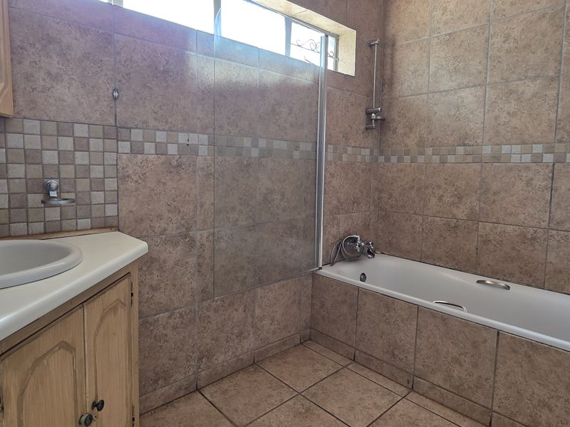 A functional bathroom featuring a built-in vanity, bathtub with shower mixer, glass screen, and full-height wall tiling.