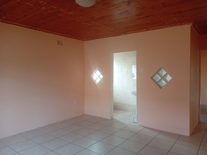 An empty bedroom featuring tiled flooring, a timber ceiling, and unique glass block accents, with direct access to an adjoining en-suite bathroom.
