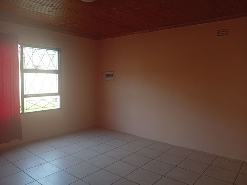 A vacant bedroom featuring tiled flooring, a timber-clad ceiling, and a window fitted with security bars.