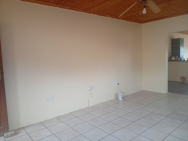 An empty living room featuring tiled flooring, a timber ceiling with a ceiling fan, and neutral walls with visible electrical points.